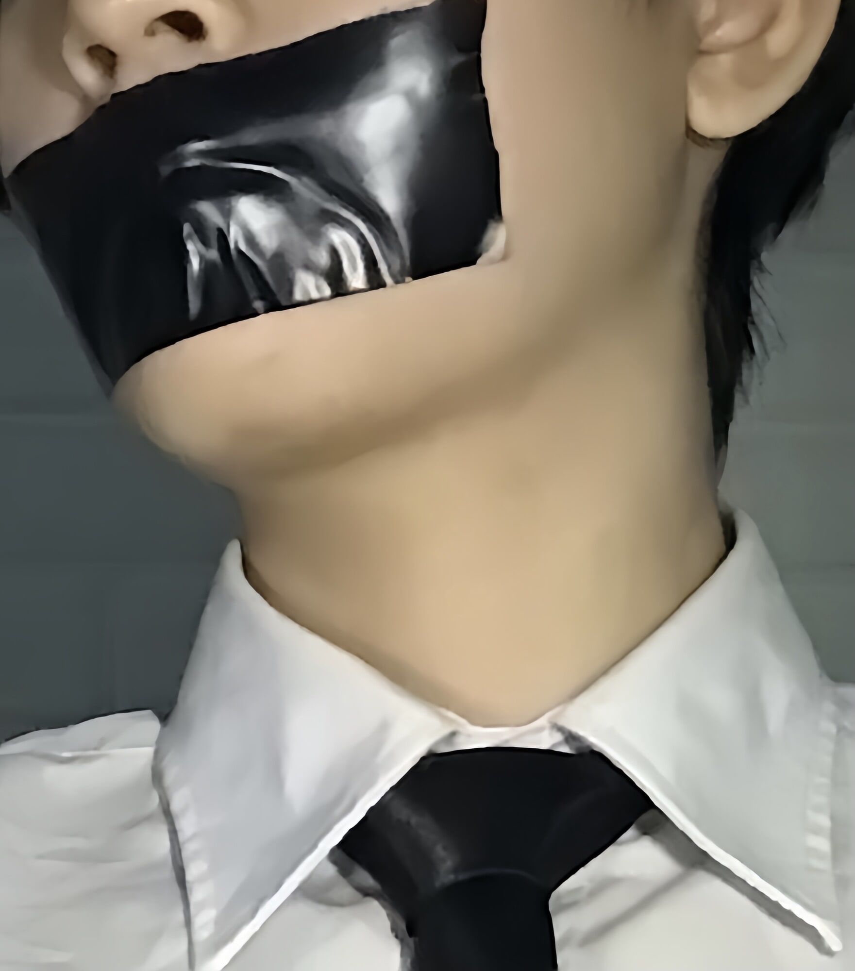 Wearing a white shirt and shiny black tie, gagged with duct 