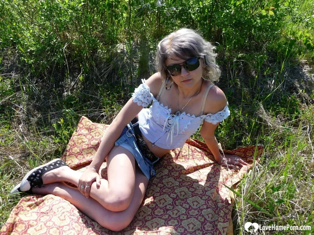 Gray-haired beauty posing naked outdoors on a blanket